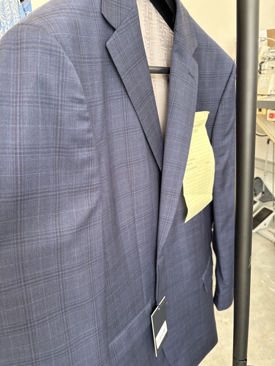A navy Prince-of-Wales check suit jacket with an alteration ticket, ready for collection