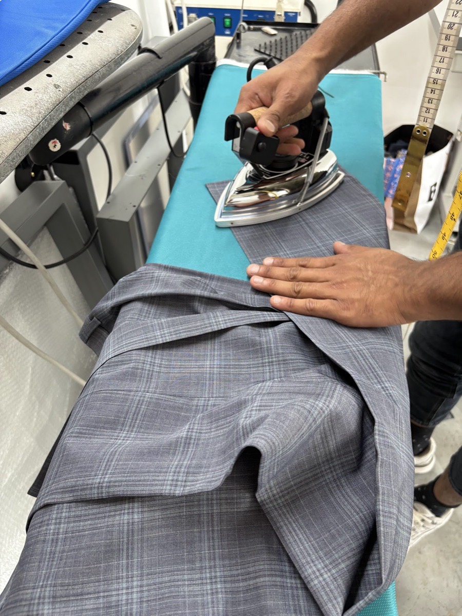Hands pressing a grey checked suit trouser with a professional steam iron at Craft Tailors